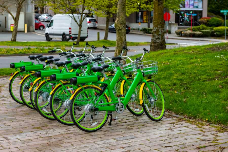 Une rangée de vélos verts électriques alignés dans un parc urbain, prêts pour la location de vélos